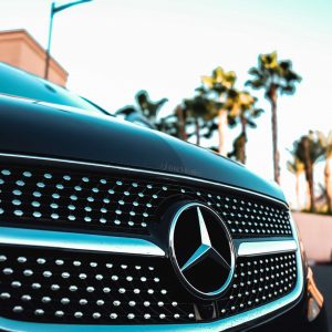 Хромированная решетка радиатора автомобиля Mercedes-Benz с логотипом на фоне пальм.